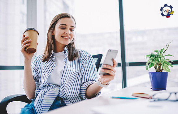 Joven Sonriente Mirando su Smartphone y Sosteniendo un Caf